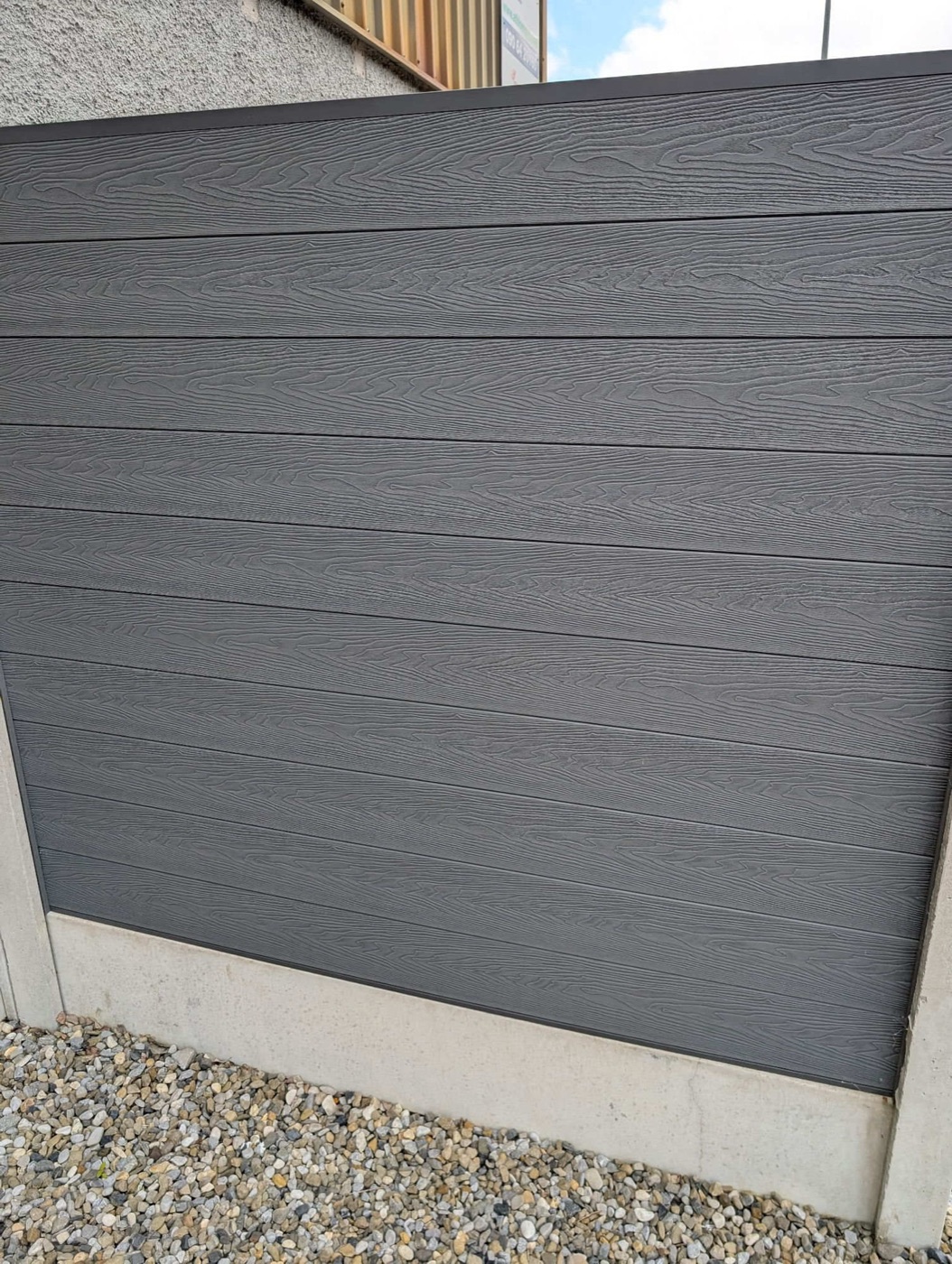 Grey wood-grain composite fence panel between concrete posts
